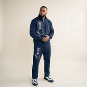 Man wearing a navy tracksuit with brand logos on a beige background