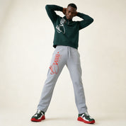 Person wearing a green hoodie and gray sweatpants with branding, standing against a plain background