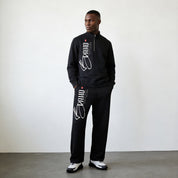 Man wearing a black tracksuit with white text and logos against a plain background