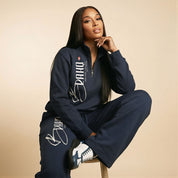 Woman wearing a navy tracksuit with visible branding on a beige background