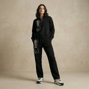 Person wearing a black tracksuit with brand logo on a beige background