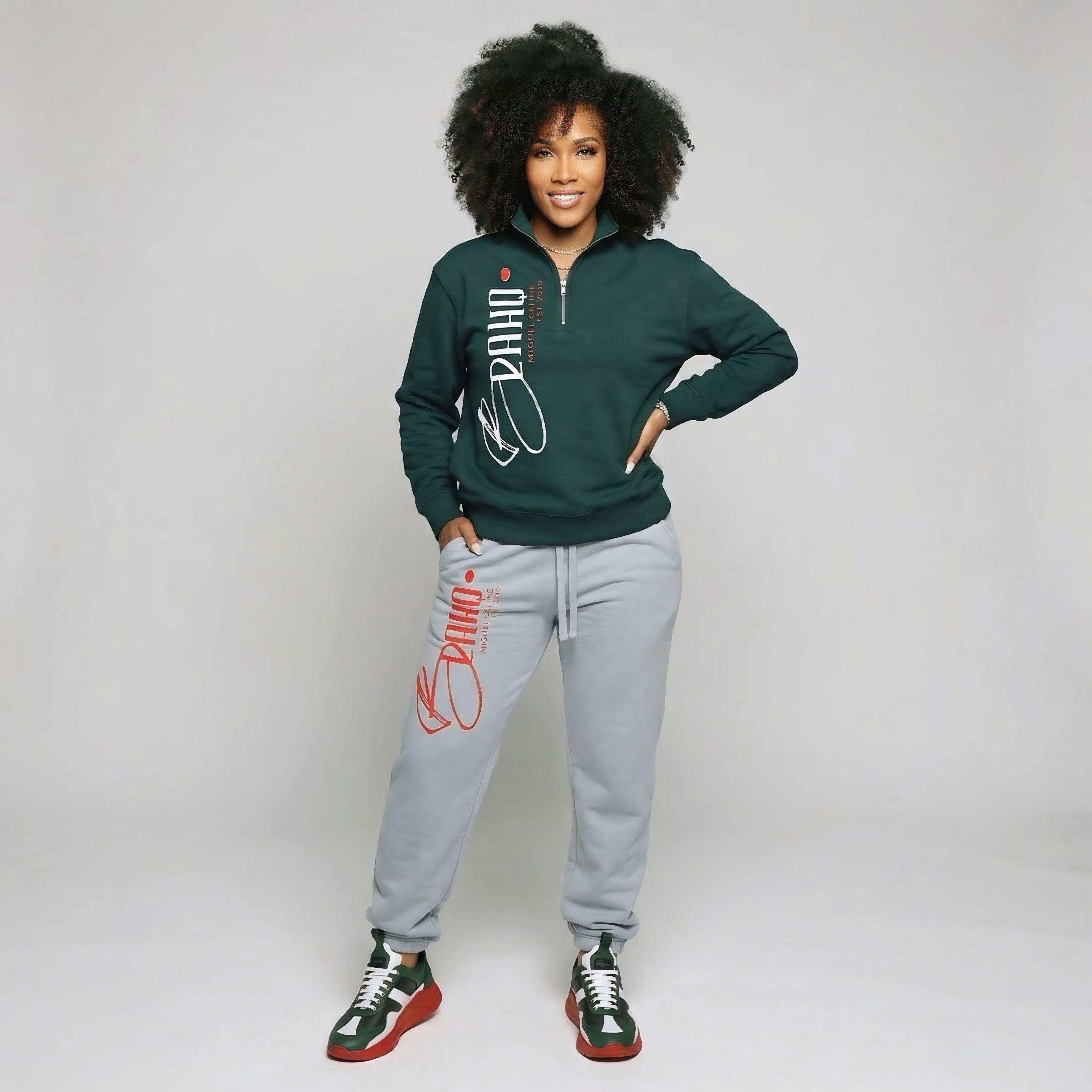 Woman wearing a green sweatshirt and gray jogger pants with red text on a plain background