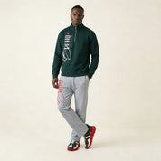 Man wearing a green jacket and gray pants with Puma branding on a beige background