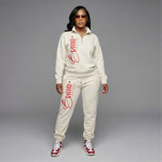 Woman wearing a cream-colored tracksuit with red branding on a gray background