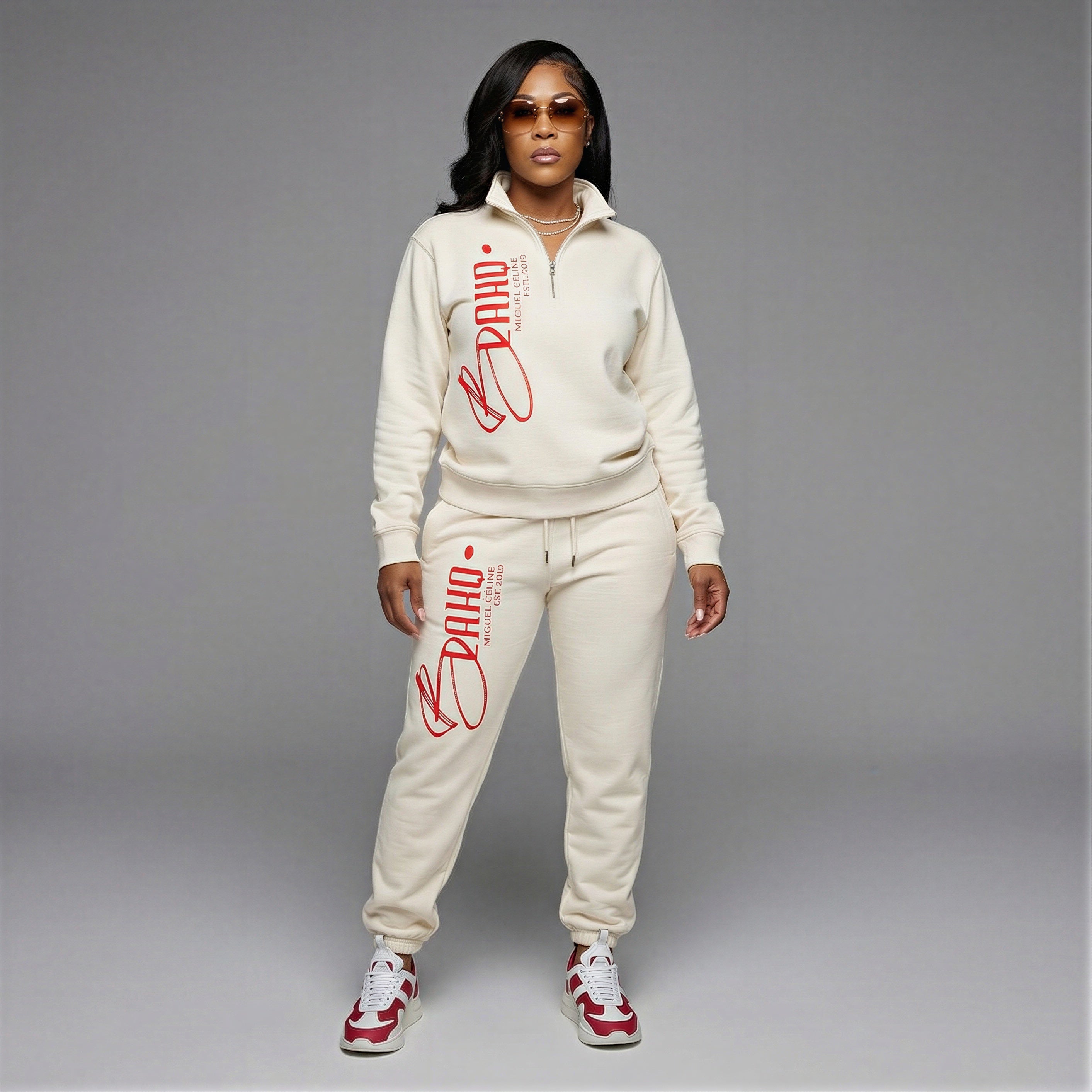 Woman wearing a cream-colored tracksuit with red branding on a gray background