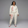 Woman wearing a cream-colored tracksuit with red branding on a gray background