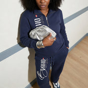 Person wearing a navy tracksuit with visible branding, holding a silver clutch.