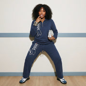 Woman wearing a navy blue tracksuit with white text, posing against a light-colored wall.