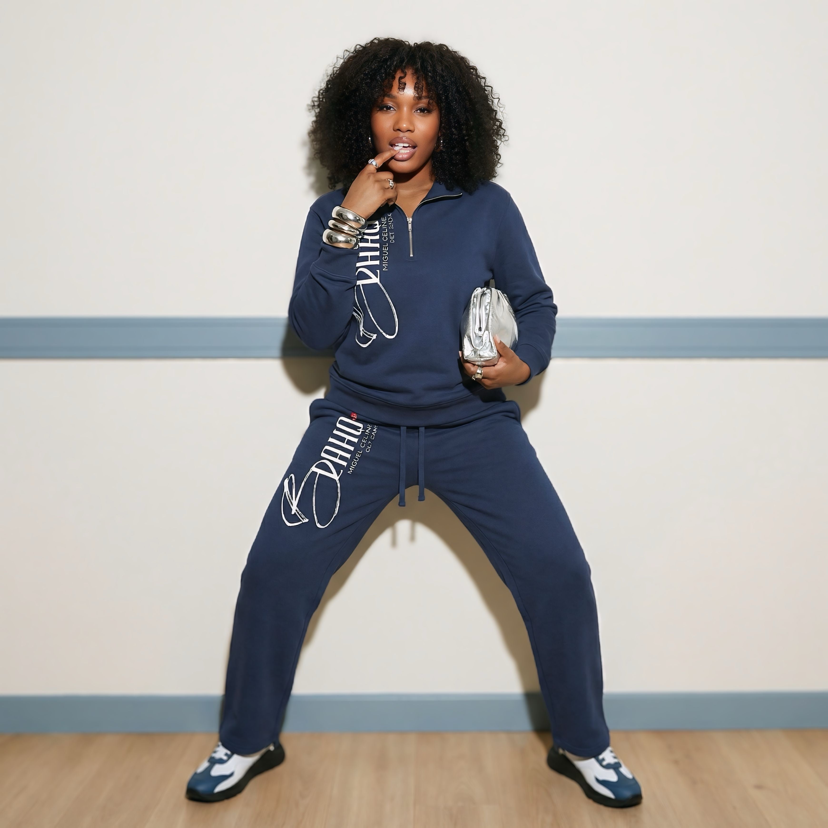 Woman wearing a navy blue tracksuit with white text, posing against a light-colored wall.