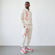 Man wearing a beige tracksuit with red branding against a white background