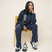 Woman sitting on a chair wearing a navy tracksuit with white accents.